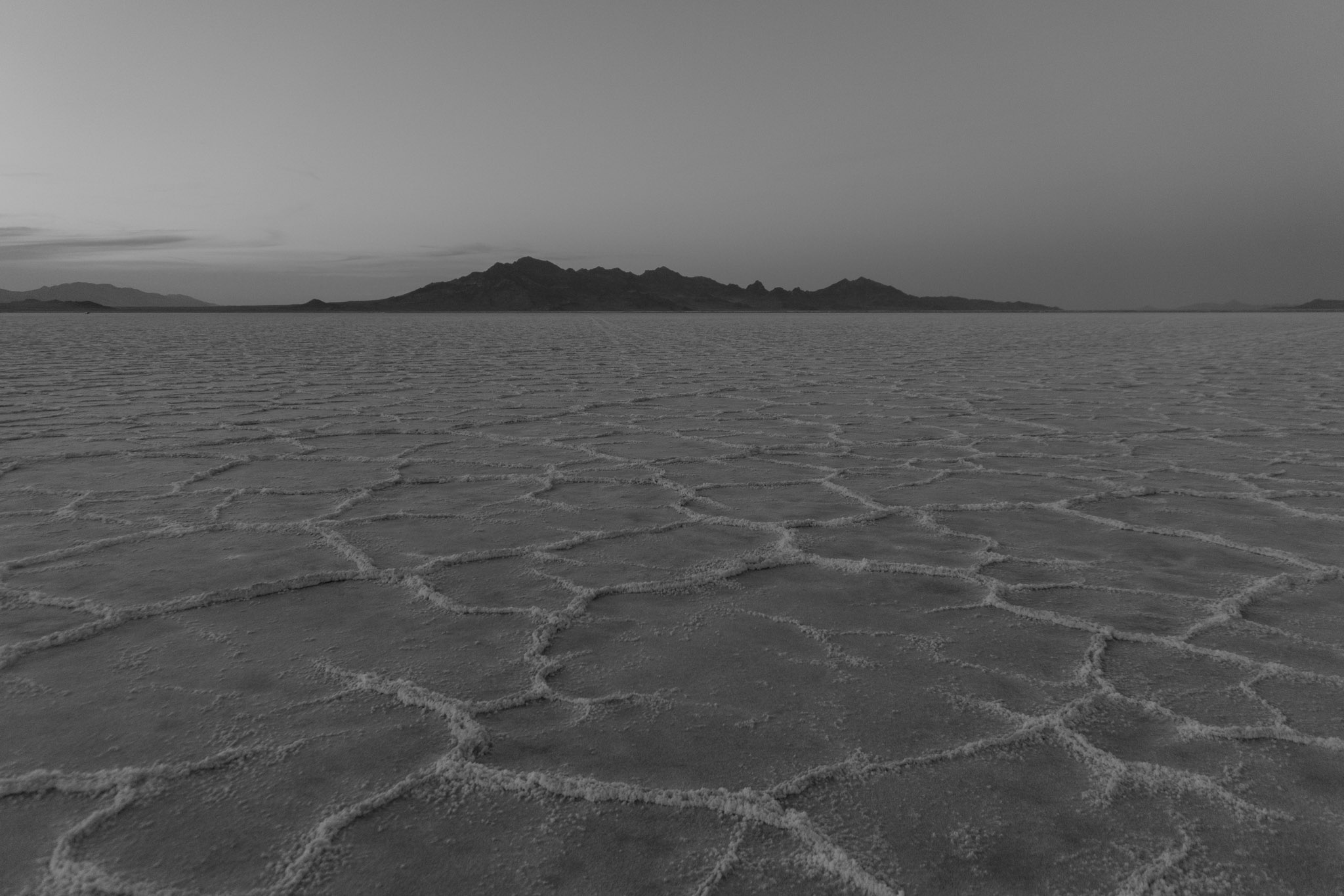 Salt flats at dusk in grayscale with dark mountains in the distance